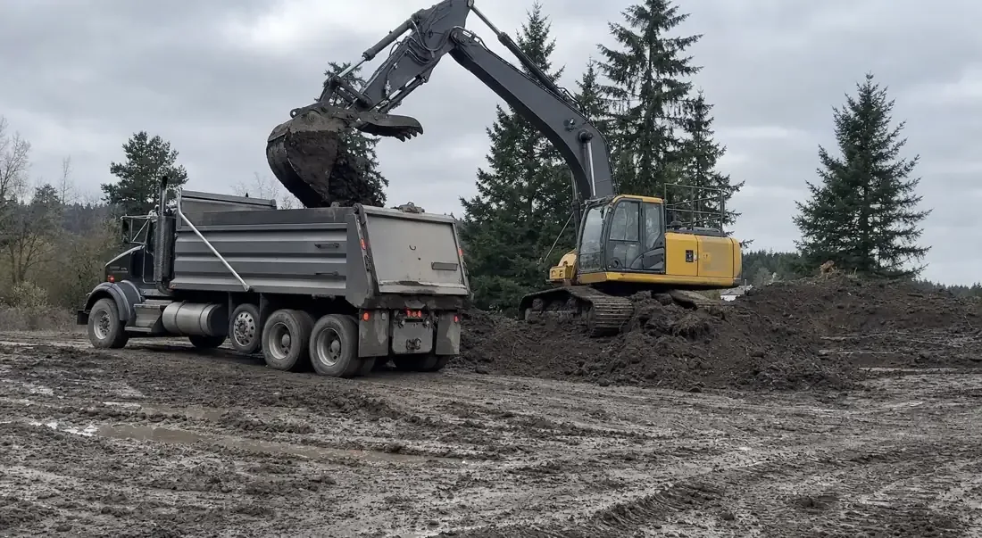 Dump truck being loaded with soil by an excavator for dirt hauling in Vancouver, WA